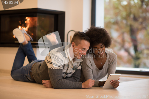 Image of multiethnic couple using tablet computer on the floor