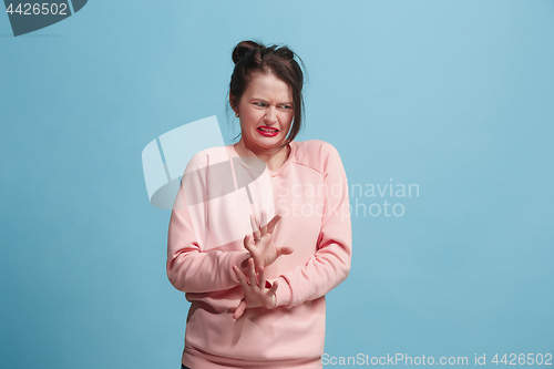 Image of Young woman with disgusted expression repulsing something, isolated on the blue
