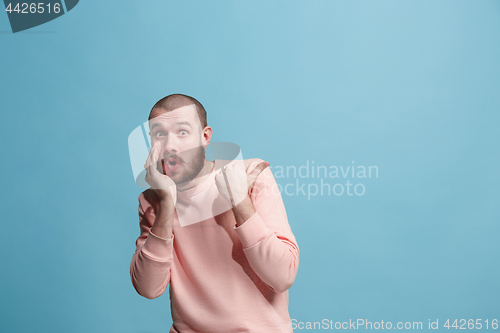 Image of The young man whispering a secret behind her hand over blue background