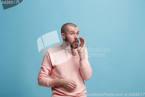 Image of The young man whispering a secret behind her hand over blue background