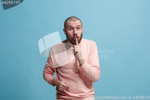 Image of The young man whispering a secret behind her hand over blue background