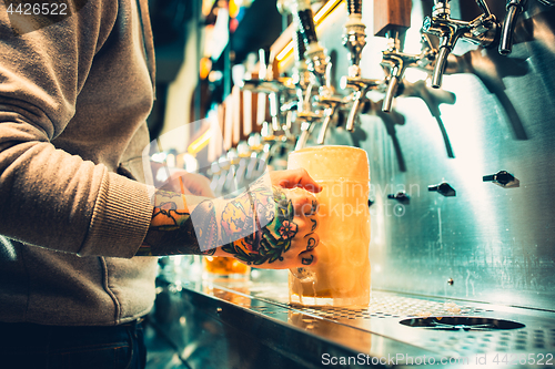 Image of Hand of bartender pouring a large lager beer in tap.