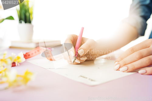 Image of The female hands holding pen. The trendy pink desk.