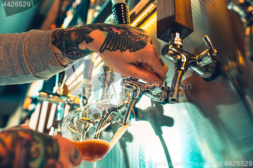 Image of Hand of bartender pouring a large lager beer in tap.