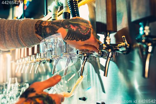 Image of Hand of bartender pouring a large lager beer in tap.