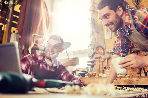 Image of two smiling carpenters with laptop at workshop