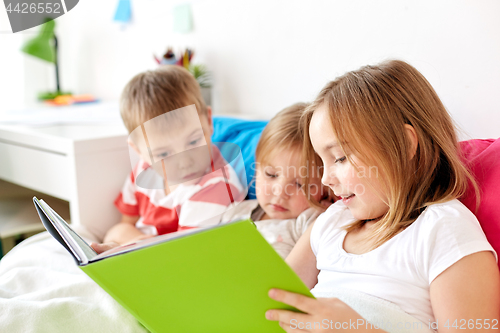 Image of little kids reading book in bed at home