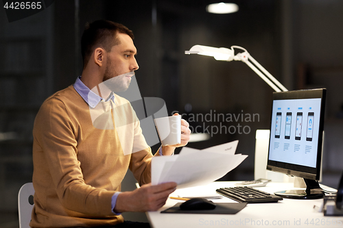 Image of man with papers and computer works at night office