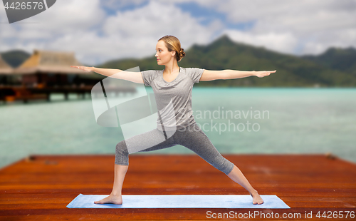 Image of woman making yoga warrior pose on mat outdoors