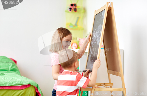 Image of happy kids drawing on chalk board at home