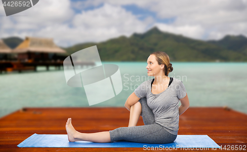 Image of woman making yoga in twist pose on mat outdoors