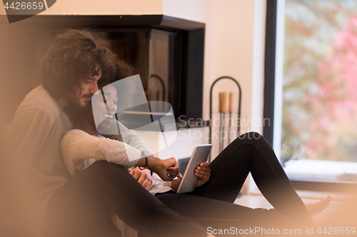 Image of multiethnic couple using tablet computer on the floor