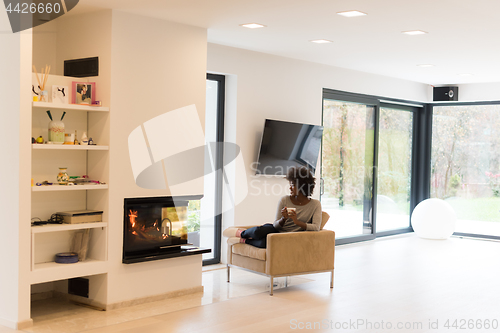 Image of black woman drinking coffee in front of fireplace