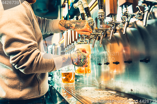 Image of Hand of bartender pouring a large lager beer in tap.