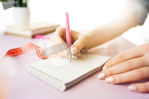 Image of The female hands holding pen. The trendy pink desk.
