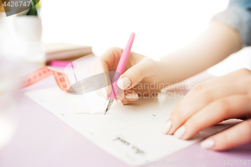 Image of The female hands holding pen. The trendy pink desk.