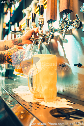 Image of Hand of bartender pouring a large lager beer in tap.