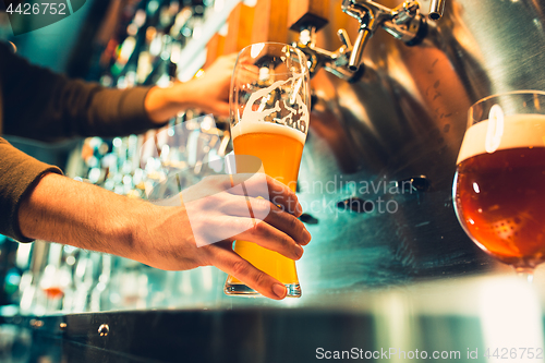 Image of Hand of bartender pouring a large lager beer in tap.