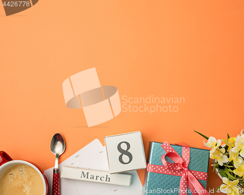 Image of The top view of orange desk with cup of coffee, gift, flowers and notebook