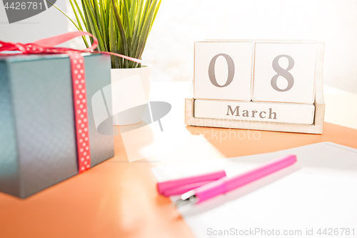 Image of The side view of orange desk with cup of coffee, gift, flowers and notebook