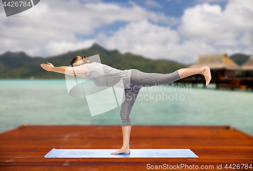 Image of woman making yoga warrior pose on mat outdoors