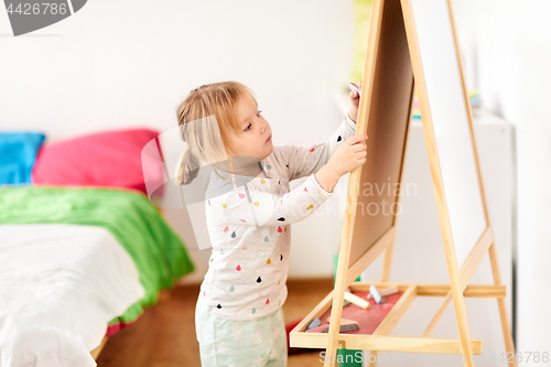 Image of happy little girl drawing on chalk board at home