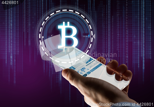 Image of hand with smartphone and bitcoin hologram