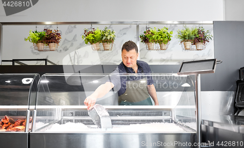 Image of male seller adding ice to fridge at fish shop