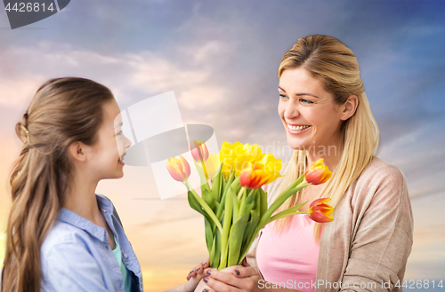 Image of happy daughter giving flowers to mother over sky