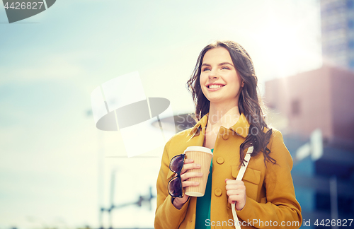 Image of happy young woman drinking coffee on city street