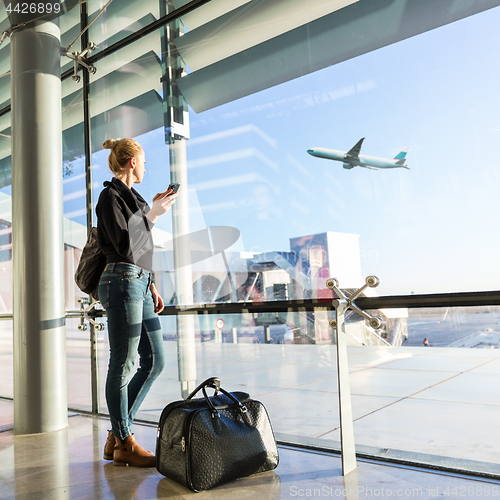 Image of Young woman waiting at airport, looking through the gate window.