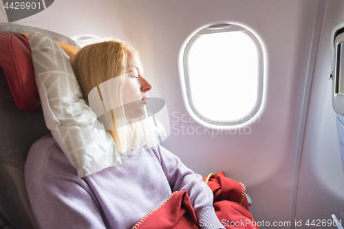 Image of Tired blonde casual caucasian lady sleepin on seat while traveling by airplane. Commercial transportation by planes.