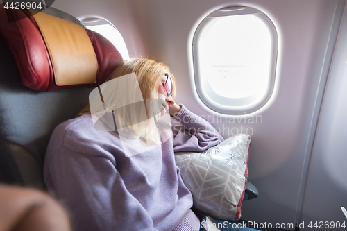 Image of Tired blonde casual caucasian lady sleepin on seat while traveling by airplane. Commercial transportation by planes.