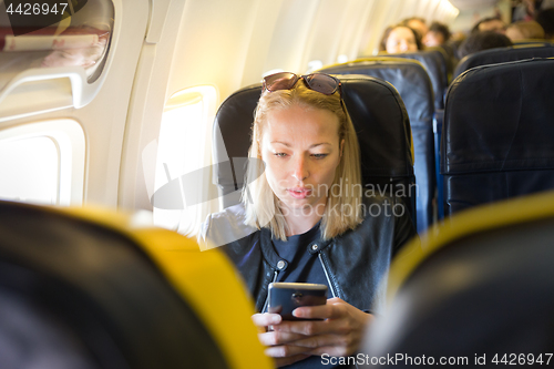 Image of Woman using mobile phone as entertainment on airplane during commercial flight.