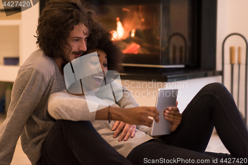 Image of multiethnic couple using tablet computer on the floor
