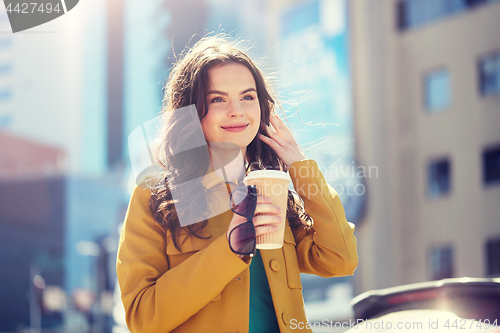 Image of happy young woman drinking coffee on city street