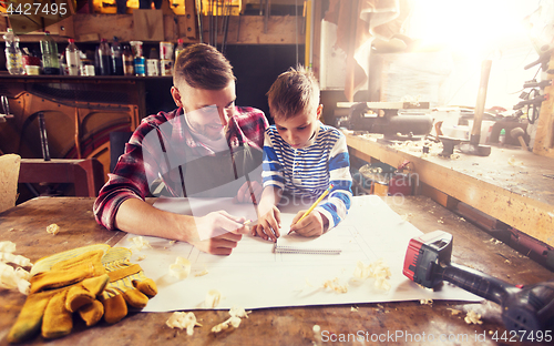 Image of happy father and son with blueprint at workshop