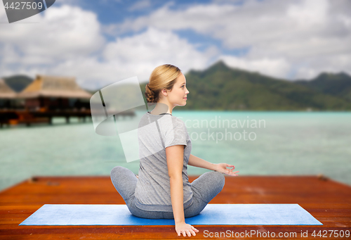 Image of woman making yoga in twist pose on mat outdoors