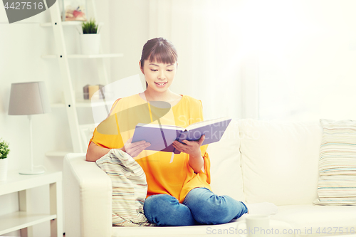 Image of smiling young asian woman reading book at home