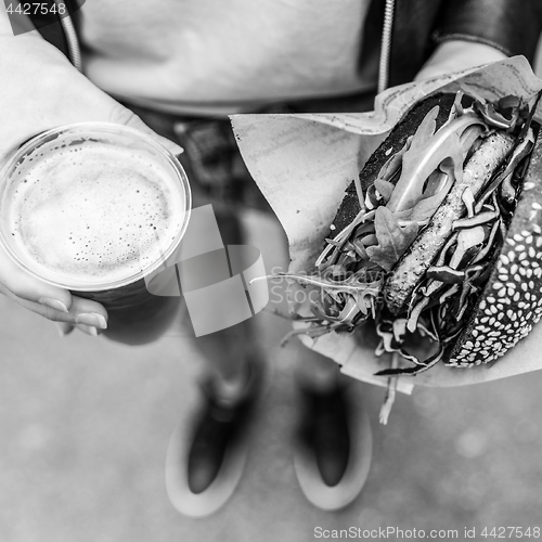 Image of Female Hands Holding Delicious Organic Salmon Vegetarian Burger and Homebrewed IPA Beer.