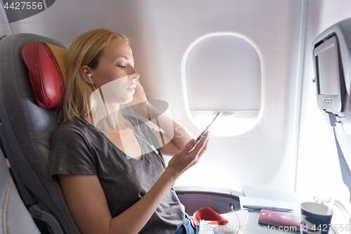 Image of Woman listening to music on smart phone on commercial passengers airplane during flight.