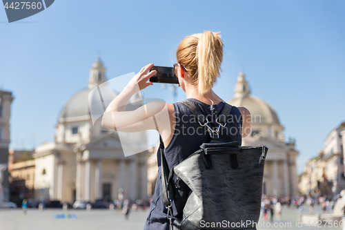 Image of Female tourist with a fashinable vintage hipster backpack taking photo of Piazza del Popolo in Rome, Italy by her mobile phone.