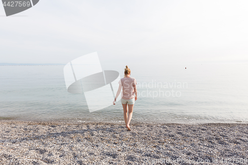 Image of Happy Carefree Woman Enjoying Sunset Walk on White Pabbled Beach.