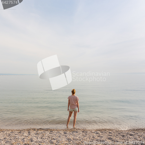 Image of Happy Carefree Woman Enjoying Sunset Walk on White Pabbled Beach.