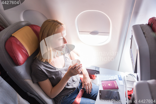 Image of Woman drinking coffee on commercial passengers airplane during flight.