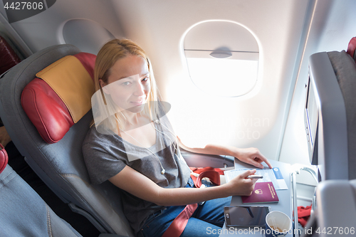 Image of Casual woman flying on commercial passengers airplane, filling in immigration form.