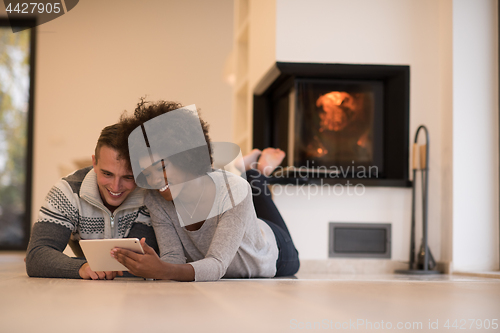 Image of multiethnic couple using tablet computer on the floor