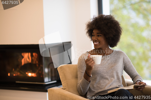 Image of black woman reading book  in front of fireplace