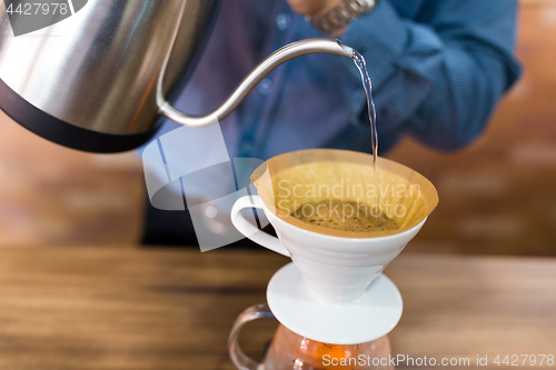 Image of Barista pouring water on coffee with filter in coffee shop