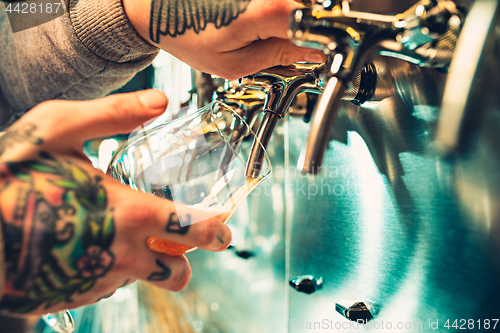 Image of Hand of bartender pouring a large lager beer in tap.